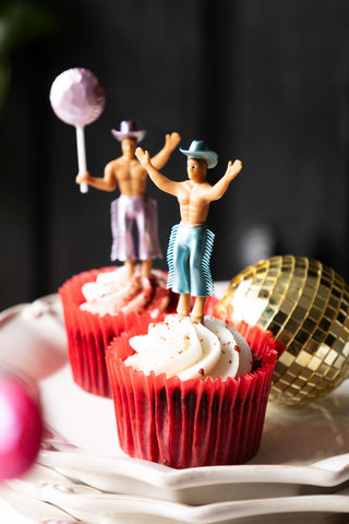 Two of the Set of 4 Cowboy Cake Toppers, styled in cupcakes on a stack of plates with a gold disco ball decoration.