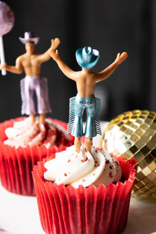 Two of the Set of 4 Cowboy Cake Toppers displayed in cupcakes, with one seen from behind revealing the name written on it.