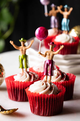 The Set of 4 Cowboy Cake Toppers styled in some cupcakes in red cases, on a table set up for a party.