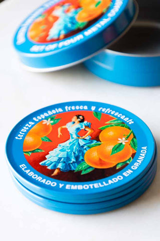 The Set of 4 Flamenco & Oranges Coasters displayed on a white table with their storage tin.