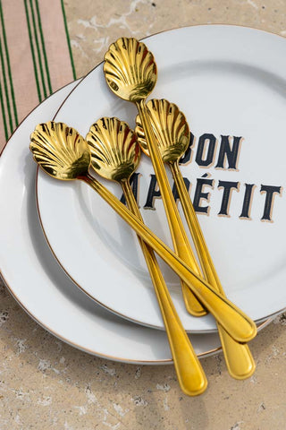 The Set of 4 Gold Shell Latte Spoons styled together on a stack of plates.