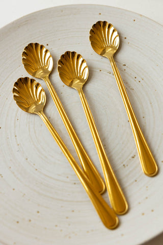 The Set of 4 Gold Shell Latte Spoons styled on a plate.