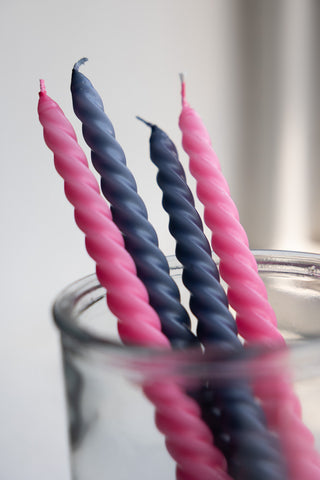 Close-up of the Set of 4 Twisted Dinner Candles in Pink & Dark Grey displayed stood in a glass container.