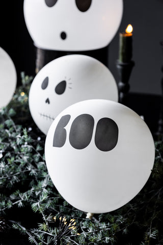 One of the Set of 5 Halloween Balloons styled on some greenery, with other balloons and a lit candle in the background.