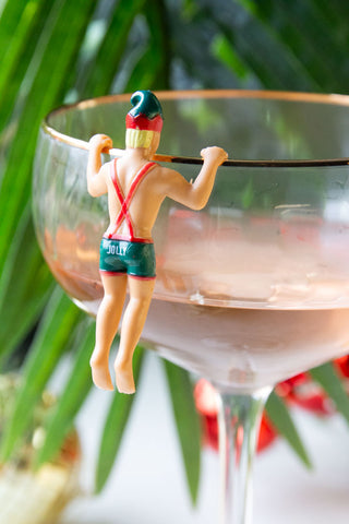 One of the Set of 6 Christmas Elf Cowboy Drink Markers styled on the edge of a champagne glass with a plant in the background.