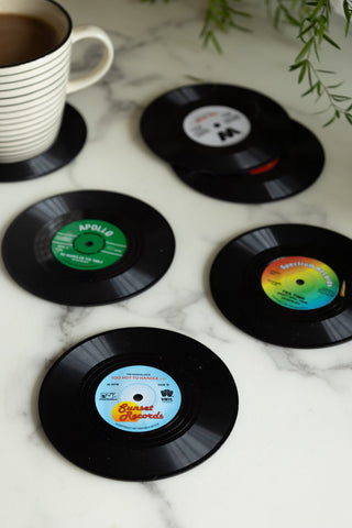 The Set of 6 Vinyl Style Coasters displayed together on a marble surface with a mug and a plant.