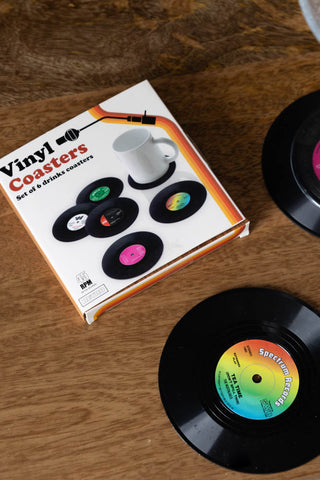 Two of the Set of 6 Vinyl Style Coasters displayed on a wooden surface along with the box.