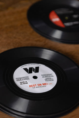 Detail shot of two of the Set of 6 Vinyl Style Coasters on a wooden table.