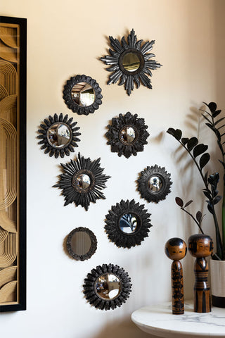 The Set of 9 Ornate Antique Black Framed Mirrors styled on a light wall with a framed artwork, above a table with a potted plant and some wooden ornaments on.