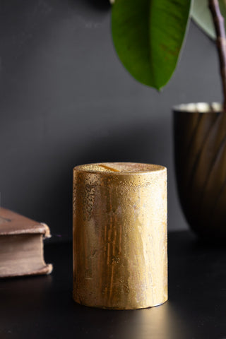 The Shiny Gold Pillar Candle - Short styled on a black surface with a book and a potted plant.