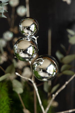 Detail shot of the Shiny Silver Bauble Spray with greenery, in front of a dark wall.