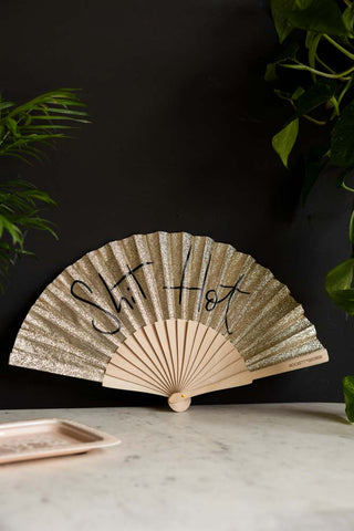 The Shit Hot Black & Gold Glitter Fan displayed leaning against a black wall, styled with a trinket tray and plants.