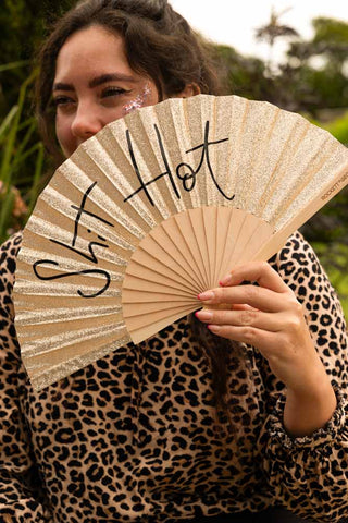 The Shit Hot Black & Gold Glitter Fan being held by a model outdoors.