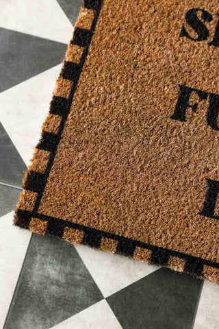 Close-up of one corner of the Shut The Fucking Door Doormat, displayed on a geometric floor.