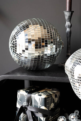 The Silver Disco Ball - 20cm styled on a black unit with a candlestick, wrapped present and other disco items.