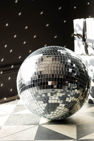 The Silver Disco Ball - 30cm styled on the floor, reflecting light onto the wall and presents behind.