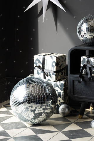 The Silver Disco Ball - 30cm styled on the floor in front of a black unit, presents and party decorations.