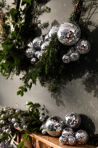 The Silver Disco Ball Cluster Christmas Decoration hung on a conifer wreath above a wooden fireplace.