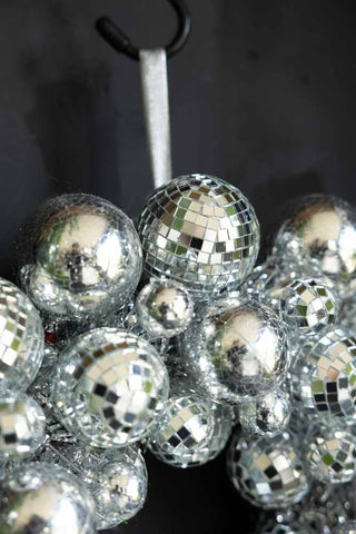 Close-up of the top and the ribbon of the Silver Disco Ball Wreath, hanging on a hook in front of a dark wall.