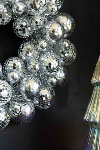 Close-up of the Silver Disco Ball Wreath in front of a black wall, styled next to a Christmas tree ornament.