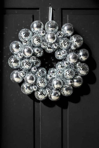 The Silver Disco Ball Wreath styled on a black door with the light casting reflections around.