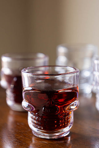 One of the Set of 4 Skull Shot Glasses styled with liquid inside, with the other glasses in the background.