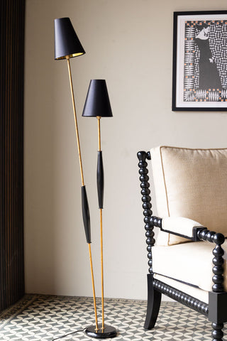 The Sleek Black & Gold Double Shade Floor Lamp in front of a neutral wall, styled with a chair and an art print.