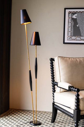 The Sleek Black & Gold Double Shade Floor Lamp switched on and displayed next to a chair and art print.