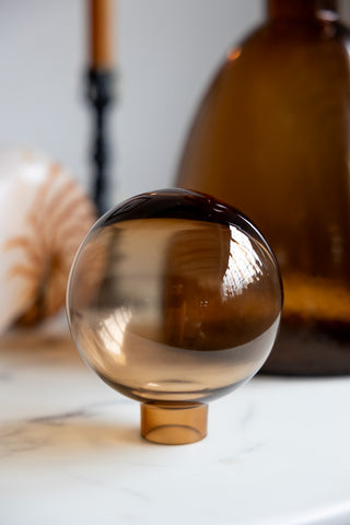 Close-up of the spherical lid of a bronze glass bottle, displayed on a white surface.