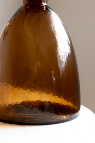 Close-up of the base of a bronze glass bottle on a white surface.