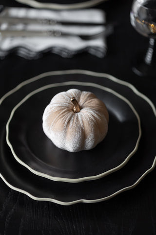 A Small Cream Velvet Pumpkin styled on a stack of two black plates on a table.