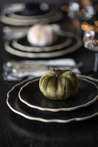 The Small Green Velvet Pumpkin styled on two black plates as part of a tablescape.