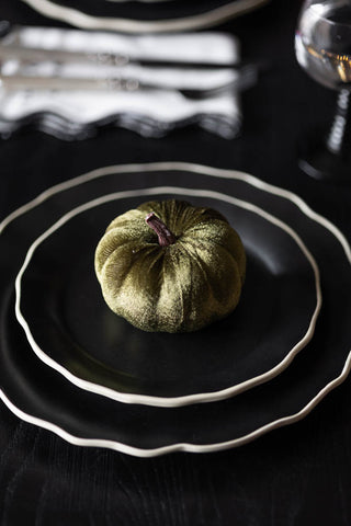 The Small Green Velvet Pumpkin styled on a stack of two black plates on a dark table.