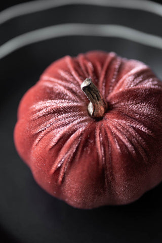 The Small Dusky Rose Velvet Pumpkin seen from above, styled on some dark plates.