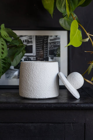 The Small Textured Jar with the lid off, displayed on a black surface with a photo in a frame and some greenery.