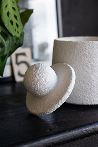 Close-up of the lid of the Small Textured Jar, styled leaning against the jar on a dark surface with a photo frame and some greenery in the background.