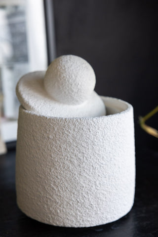 The Small Textured Jar with the lid on at an angle, displayed on a dark surface with a photo frame and some greenery in the background.