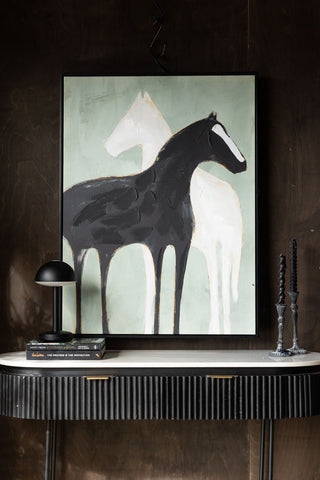 The Stallion Shadow Canvas Art Print styled on a console table in front of a dark wall, with a table lamp, books and some candlestick holders.