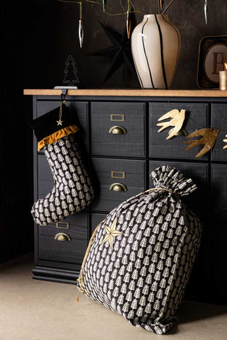 The Star Printed Christmas Sack styled with a stocking and a bird garland in front of a black and wooden unit, with various other decorative home accessories.