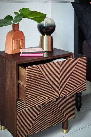 The Starburst Bedside Table with the top drawer open, styled next to a bed with a vase, table lamp and some books on the top.