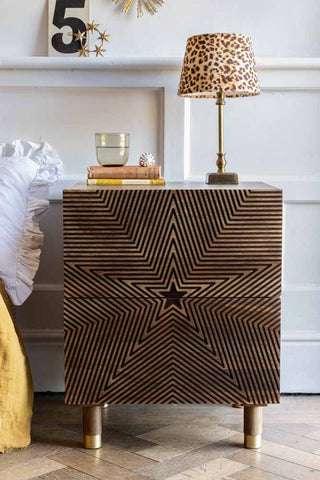 The Starburst Bedside Table seen from the front, styled next to a bed with a lamp and various home accessories on top.