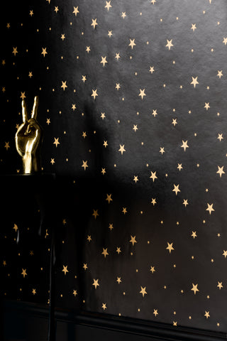 Black and god star print wallpaper displayed on a wall behind a table with a gold peace hand ornament on.