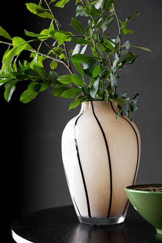 The Statement Black & White Swirl Vase displayed with branches inside, styled on a black table alongside a green bowl.