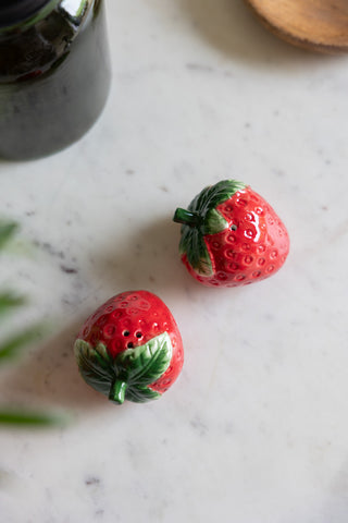 The Strawberry Salt & Pepper Shakers seen from above, styled on a marble surface with other kitchen accessories.