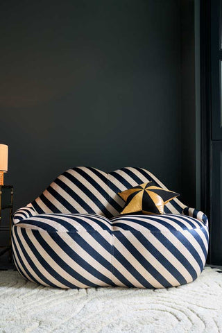 The Stripe Lips Sofa styled with a star cushion and side table with lamp, in front of a black wall.