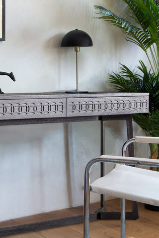 Close-up of the Stylish Mango Wood 2-Drawer Desk with a table lamp and ornament on, styled with a chair and a large plant.