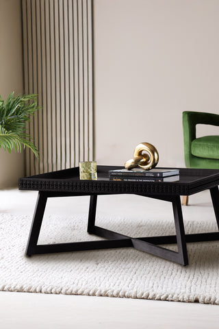 Beautiful black wooden coffee table in a neutral living room setting. Underneath the statement coffee table is a white deep pile rug. Styled on the black coffee table is a quirky ornament.