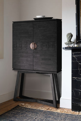 The Stylish Mango Wood Drinks Cabinet in the corner of a room with plates on top, styled with a rug next to a fireplace with an ornament.