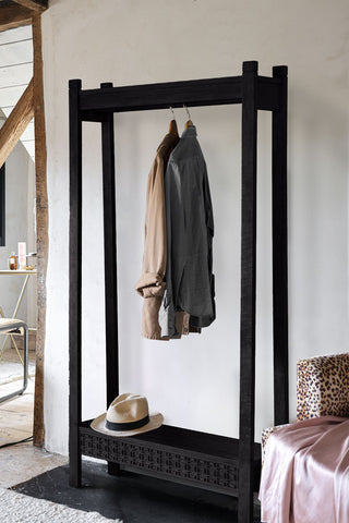 The Stylish Mango Wood Freestanding Open Wardrobe styled with some clothes and a hat on, displayed in front of a plain wall next to a chair.