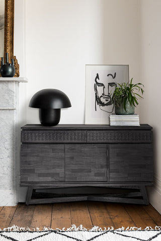 The Stylish Mango Wood Multi-Drawer Sideboard styled in the corner of a room, with a lamp, stack of magazines, book and an art print.